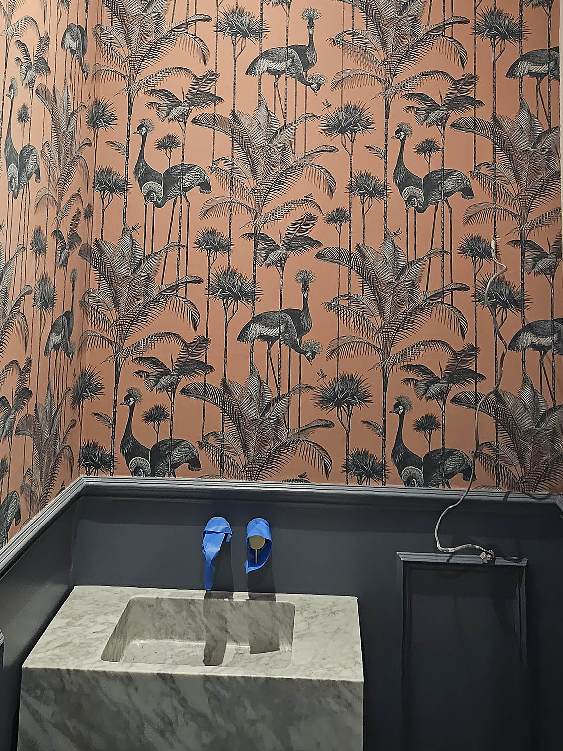 Red- orange wallpaper with flamingos and tropical plants wallpaper installed in a bathroom.