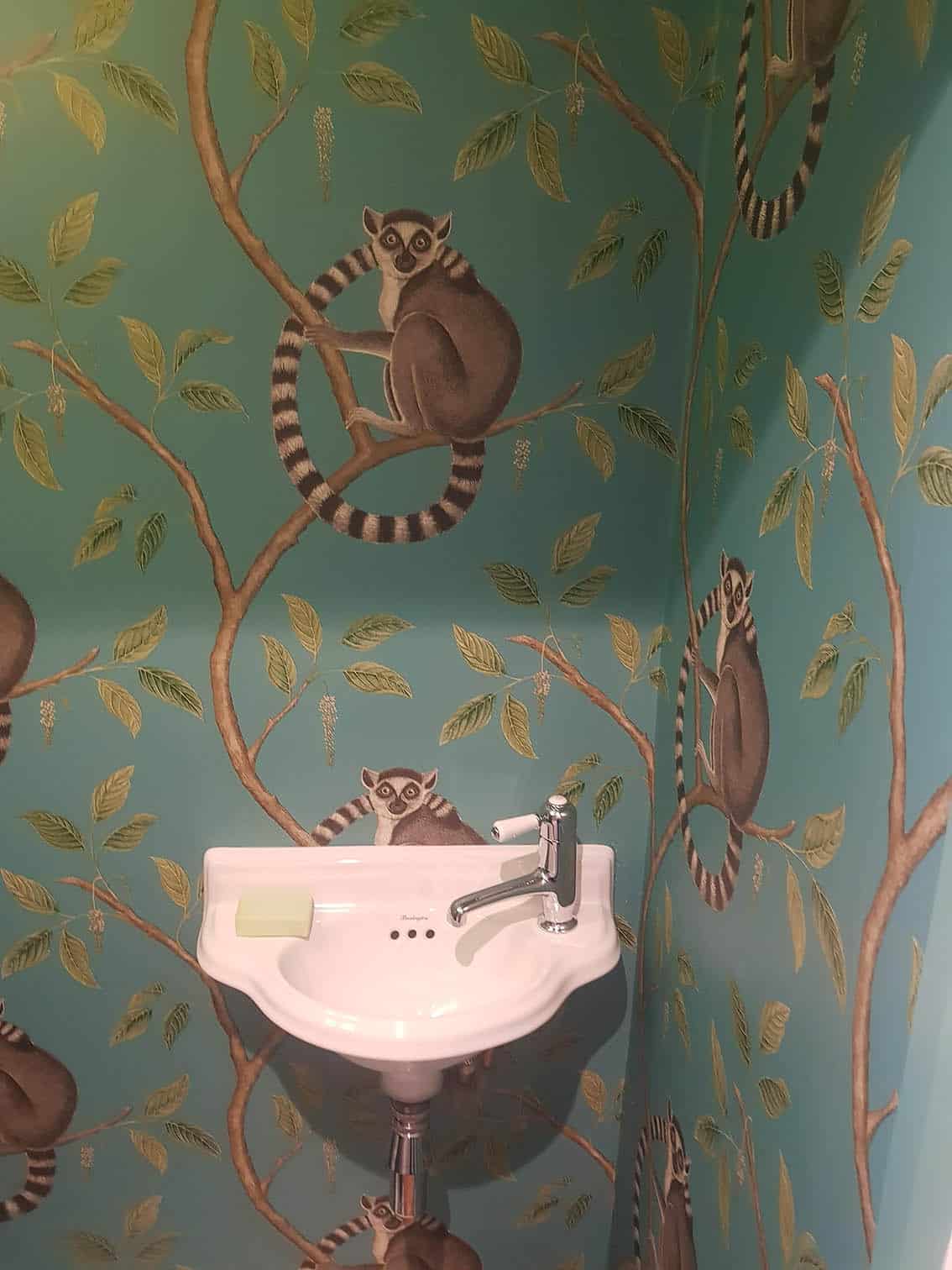Sanderson Ringtailed Lemurs wallpaper professionally installed in a bathroom. Wallpaper has green background and animated lemurs .