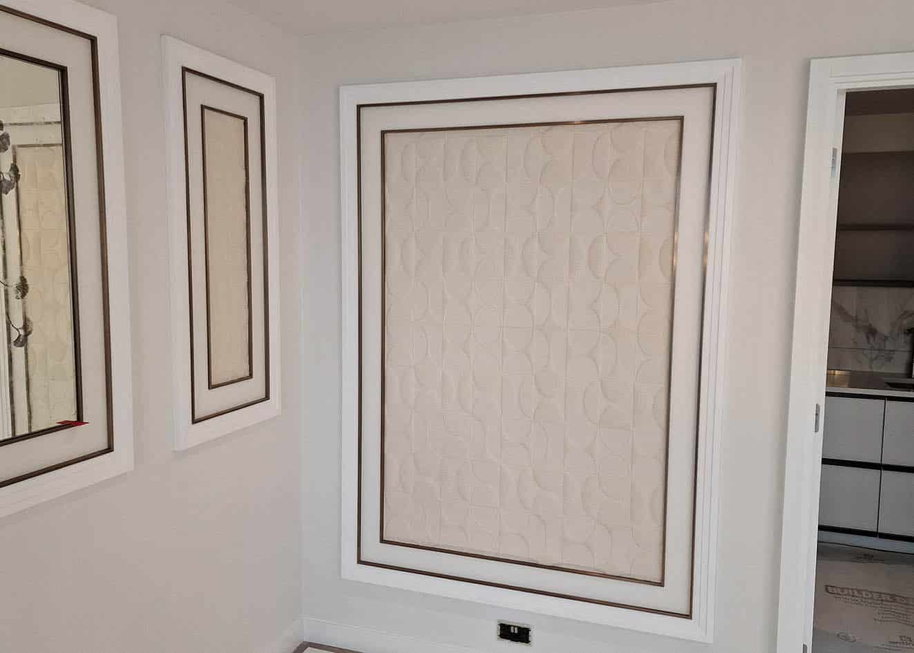 Arte Curve wallpaper installed in frames. The wallpaper is white and patterned. There are two frames ,one of them is larger and a mirror decorated with flowers and butterflies in dark grey on the reflective part.