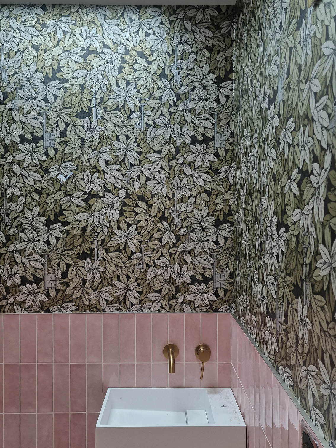 Cole and Son ` Chiavi Segrete wallpaper professionally installed in a bathroom. The wallpaper has green leaves pattern and is combined with pink tiles.