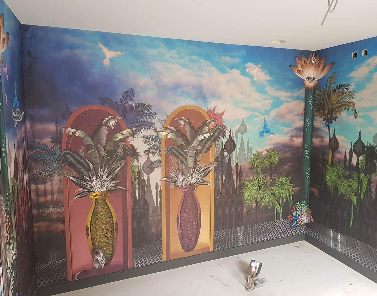 Colourful Tektura made to measure wall mural with trees and exotic plants and blue sky with white clouds on a wall.