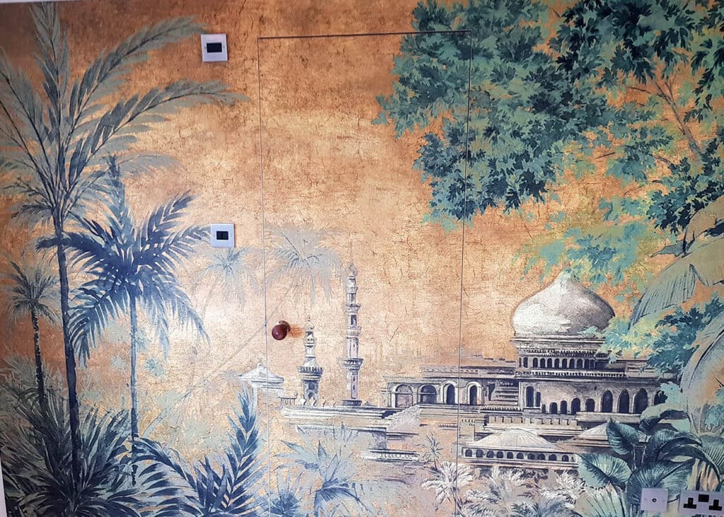 Made to measure Coordonné RANDOM CHINOISERIES TAJ MAHAL installed in a bedroom. Background is orange and is a drawing of Taj Mahal and palm trees. There is a door in the middle wallpapered .