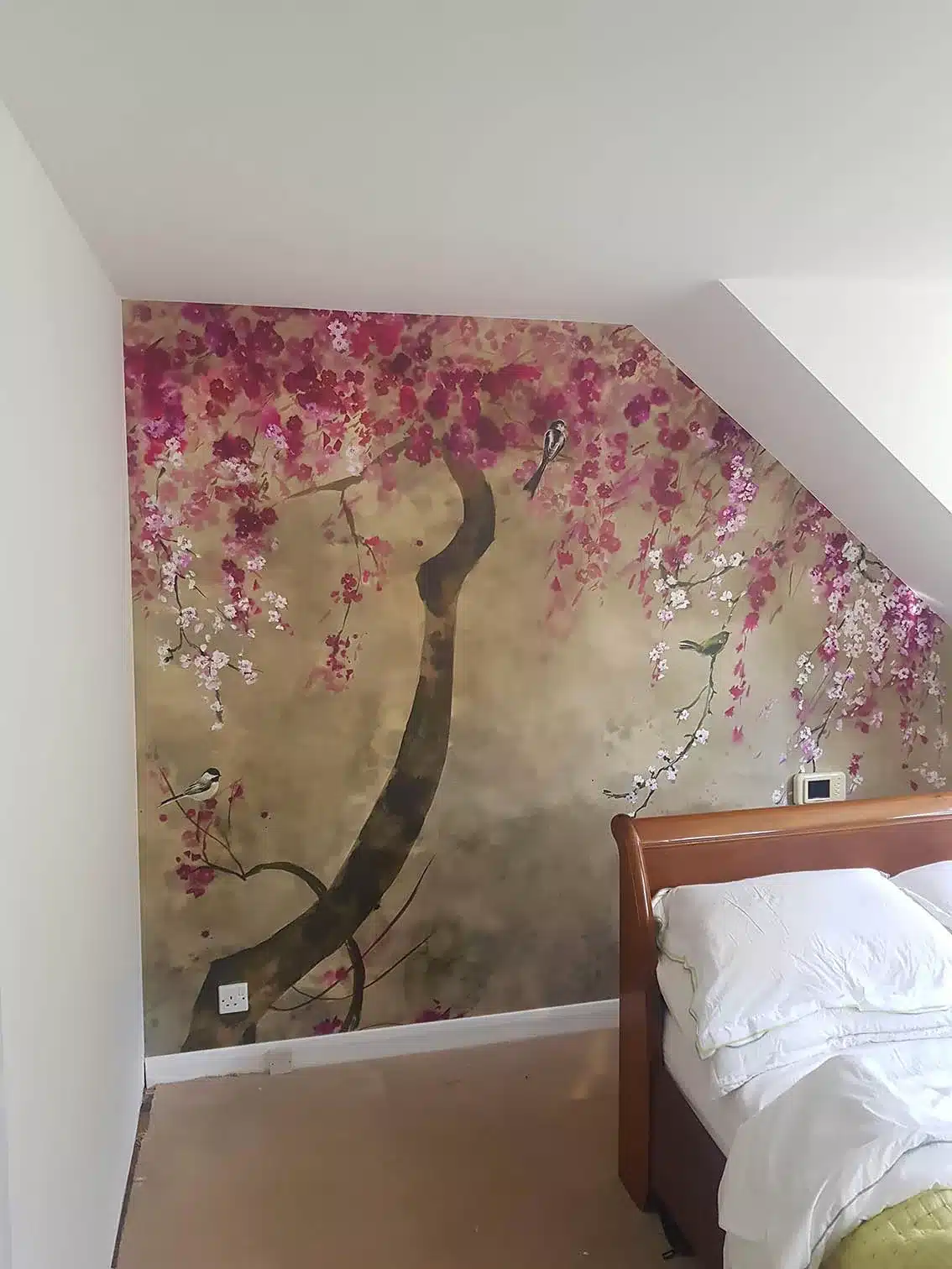 Wallpaper mural professional wallpaper hanging. A tree with pink flowers and birds in a bedroom.