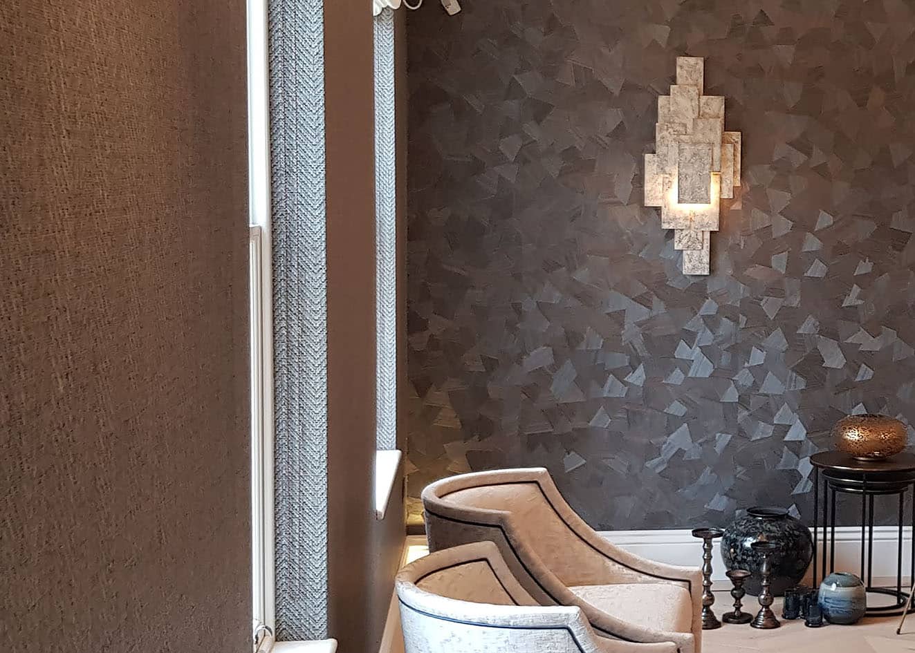 Omexco wallcovering on a wall with a light next to white armchairs in a luxury bedroom in Chigwell.