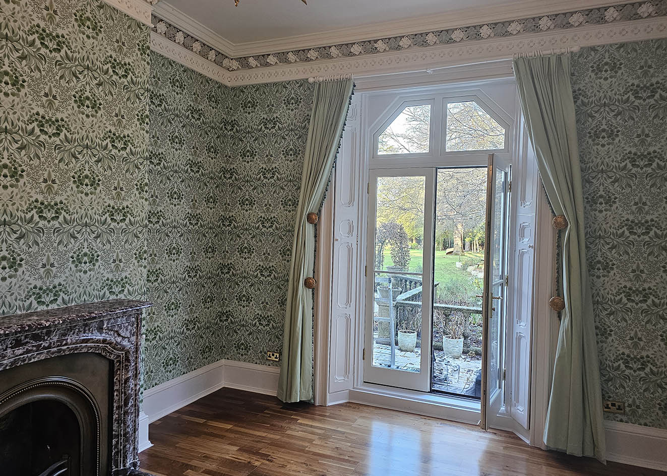 green-and-white-wallpaper-installation-London Wallpaper in green and white installed in large room with tall window and a mantelpiece.