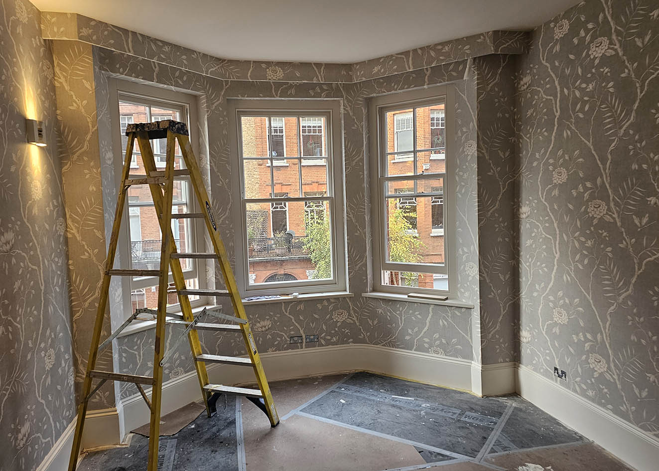 wallpaper-hanging-W11 Wallpaper hanging next to a window. The wallpaper is dark beige colour with plants and flowers. The project is in W11, London.